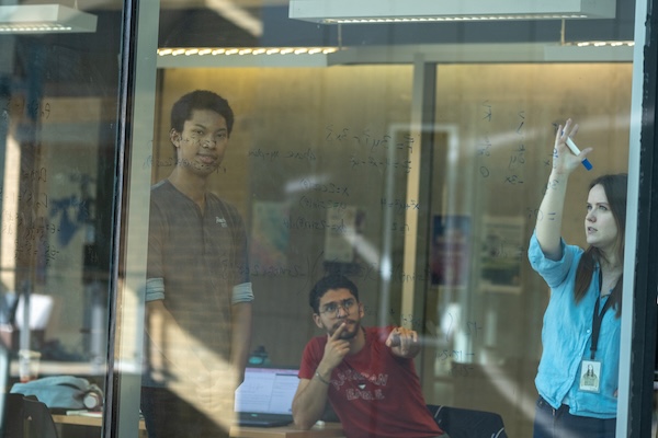 Rahman solving an engineering problem on a whiteboard with two other students