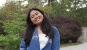 Student in a blue shirt stands in a garden.