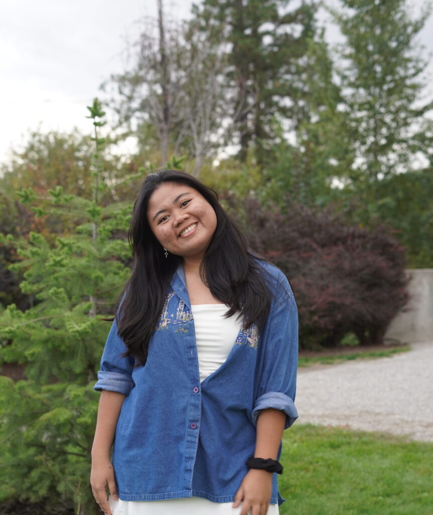 Student in a blue shirt stands in a garden.